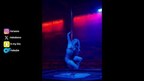 Media: Video of a blonde woman in a blue bikini performing a pole dance in a dimly lit, purple-lit nightclub, surrounded by red and blue neon lights.