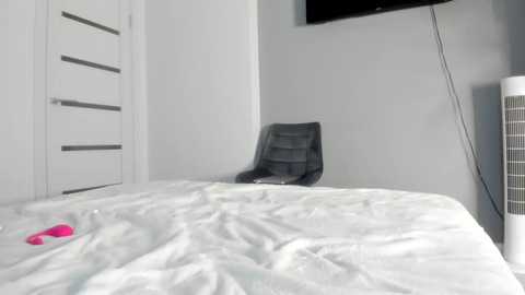 Media: Video of a minimalist bedroom with a white bed, gray chair, and a mounted TV on the wall, featuring a sleek, modern design.
