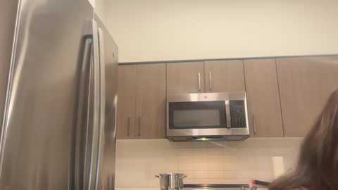 Media: Video of a modern kitchen with stainless steel appliances, including a large refrigerator on the left, a microwave oven and hood fan above a beige tile backsplash.