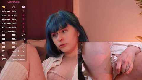 Media: A video of a young woman with blue hair, wearing a white shirt and beige lingerie, sitting on a bed. The background shows a digital camera viewfinder with stats.