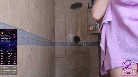 Media: A video of a beige-tiled shower, with a person wrapped in a lavender towel standing on the right. A digital display on the left shows a weather forecast.