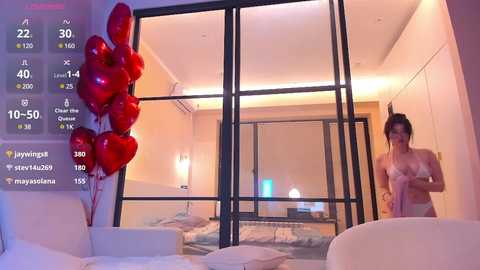 Media: Video of a modern bedroom with a white bed, heart balloons, and a topless woman with large breasts.
