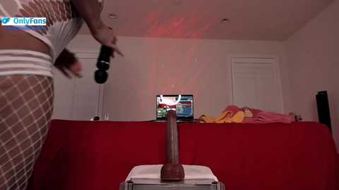 Media: Video of a woman in white lingerie, holding a dildo, standing in front of a red couch with a TV showing a video.