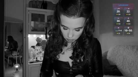 Media: A black-and-white video of a woman with curly hair, wearing a leather jacket, looking at a mirror. The background shows a cluttered room with a TV displaying a game screen.