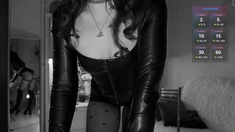 Media: A black-and-white video shows a woman in a tight leather outfit bending over, revealing cleavage. She has long, wavy hair and wears a choker. A weather forecast is displayed in the background.