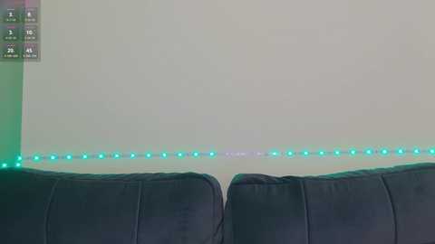 Media: A video of a dark gray couch with a soft texture, featuring a glowing line of green LED lights along the wall behind it. The background is a plain, light beige wall.