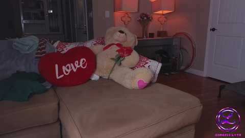 Media: Video of a cozy living room with a beige sofa, plush teddy bear holding a red rose, heart-shaped pillow, and \"Love\" written on it.