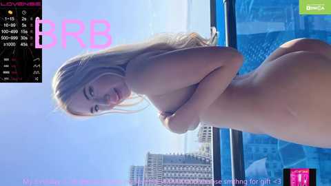 Media: Video of a nude, slender, fair-skinned, blonde woman with small breasts, smiling, standing in front of a pool with blue water and a cityscape background.