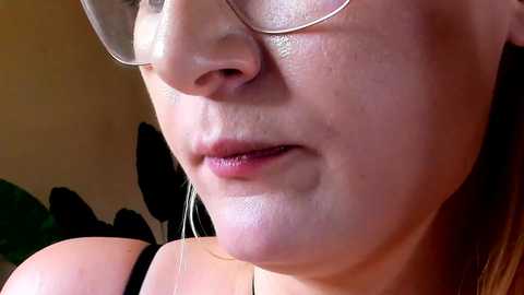 Close-up video of a Caucasian woman with fair skin, wearing glasses and a black top, focusing on her nose and mouth. She has a neutral expression.