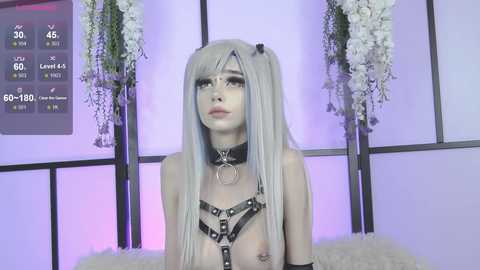 Media: Video of a pale-skinned, androgynous person with long, straight, platinum-blonde hair, wearing a black leather harness and choker, standing in front of a purple-lit, floral backdrop.