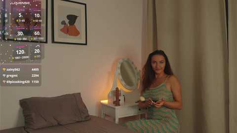 Media: A video of a woman in a striped pajama set sitting on a bed, holding a phone, in a dimly lit bedroom with a white vanity mirror and framed artwork on the wall.