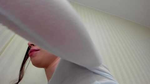 Media: Video of a young woman with light skin, wearing a white T-shirt and pink lipstick, holding a white sock in the foreground. She has long brown hair. Background shows a plain white wall.