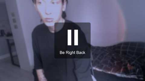 Media: A video of a man in a black shirt, blurred, with a black and white bed in the background. Text overlay: \"Be Right Back.\