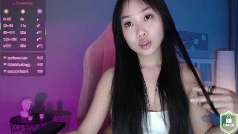 Media: A video of an East Asian woman with long black hair, wearing a white strapless top, sitting in a dimly lit room with purple and blue lighting. She has a neutral expression and is holding her hair.