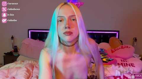 Media: A video of a topless, fair-skinned, platinum blonde woman with light blue and pink highlights, wearing a choker, in a brightly lit bedroom with neon lighting, pink bedding, and colorful plush toys.