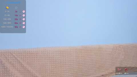 A video of a sandy beach with a blue sky background. The sand is smooth and light brown, extending horizontally. In the top left corner, a smartphone screen displays a weather app with icons and text.