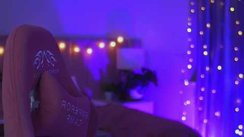 Media: Video of a dimly lit bedroom with purple and blue lighting, featuring a person's arm tattooed with \"Fortnite\" and a blurred background of fairy lights and a window.