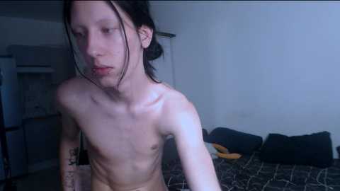 Media: Video of a thin, Asian man with long black hair and pale skin, shirtless, in a dimly lit bedroom with a bed, pillows, and a white wall.
