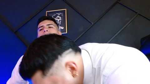 Media: Video of a man with short black hair, medium build, wearing a white shirt, leaning forward, viewed from below, in a dimly lit room with black walls and a framed picture.