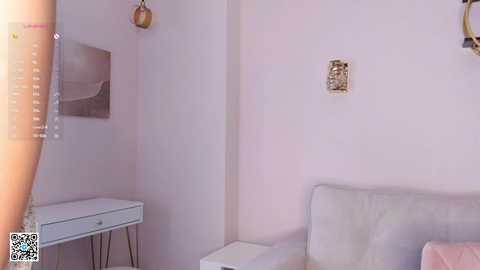 Media: Video of a minimalist, pastel-colored bedroom with a white bed, a small white desk, a framed abstract painting, and two hanging pendant lights, creating a serene, modern ambiance.