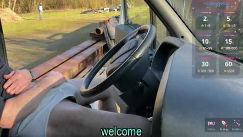 Media: Video of a dilapidated truck interior, with a rusted steering wheel and dashboard. A person's arm wearing a gray shirt is visible on the left. Outside, a grassy field with a tree line and a person walking. Text overlay reads \"welcome.\