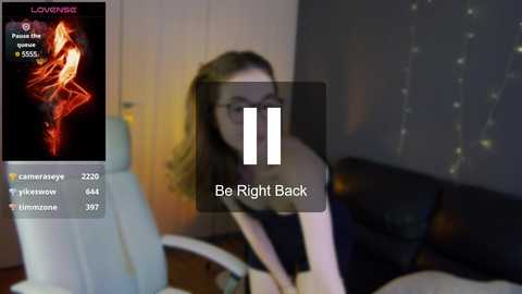 Media: A blurry photo of a woman in glasses, wearing a dark top, sitting on a bed with white sheets and a dark headboard. A \"Be Right Back\" text overlay.