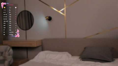 Media: Video of a modern, minimalist bedroom with a beige headboard, gray pillows, and a wooden nightstand. A circular mirror and gold geometric patterns adorn the walls, with a pink floral overlay.