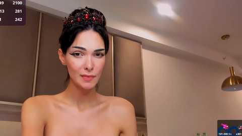 Media: Video of a topless woman with olive skin and dark hair adorned with a jeweled crown, in a modern kitchen setting, with virtual reality overlay.