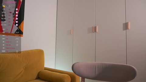 Media: A minimalist, modern living room video featuring a mustard-yellow sofa, a sleek grey armchair, and a white wall with a colorful abstract painting and a minimalist, modern light fixture.