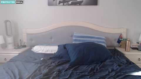Media: Video of a neatly made bed with a light wood headboard, blue and white bedding, and a nightstand with a lamp, phone, and a water bottle.