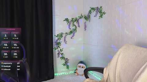 Media: A video of a cozy corner with a plush penguin, faux ivy wall, soft beige chair, and a black curtain, lit by soft blue-green fairy lights.