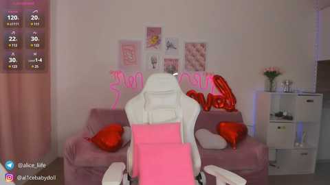 Media: Video of a pink gaming chair with red heart pillows, positioned in a cozy, pink-themed room with a white wall, heart-shaped lights, and a white shelf.