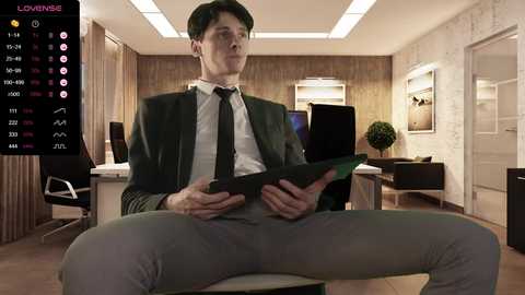 Media: Video of a man in a gray suit and tie sitting with legs apart, holding a tablet in a modern office with wooden walls and chairs.