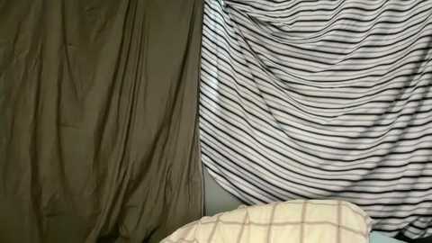 Media: Video of a tent interior with a beige canvas wall and a striped black and white wall. A beige and white checkered pillow is visible at the bottom.
