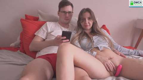Media: A video depicts a young couple, a man in glasses and a woman with long hair, lying on a bed with red and gray pillows.