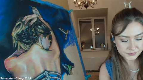 Media: Video of a young woman with brown hair, wearing a blue top, admiring a detailed, colorful painting of a woman in a blue dress on a blue background.