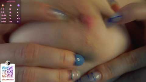 Media: A video shows a close-up of a hand with blue nail polish, holding a soft, pink object. The background is blurred, with a calendar displaying \"LOUISSE\" and \"GOALIES\" in the top left corner.