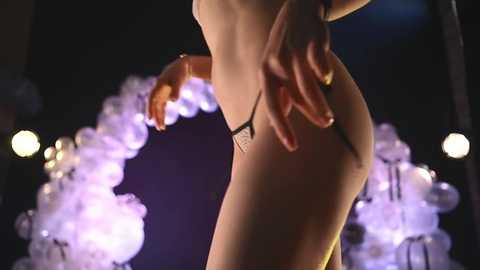 Media: Video of a partially nude woman with fair skin, wearing a black thong, posing in a dimly lit room with purple and white smoke effects.