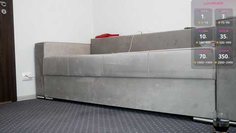 Media: Video of a minimalist, modern living room with a grey sectional sofa against a white wall, featuring a virtual reality interface overlay displaying health stats and game options.