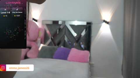 Media: Video of a modern, minimalist bedroom with a mirrored wall reflecting a bed with colorful pillows, white sheets, and a pink teddy bear.