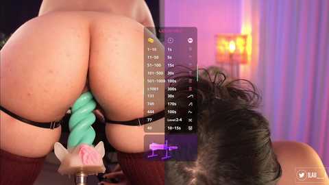Media: Video of a person with fair skin, wearing a green, spiral dildo, and black garter belt, bent over a massage table, in a dimly lit room with purple and pink lights.