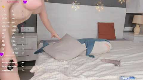 Media: Video of a nude woman with fair skin, medium-sized breasts, and a slender physique, lying on a bed in a modern bedroom.