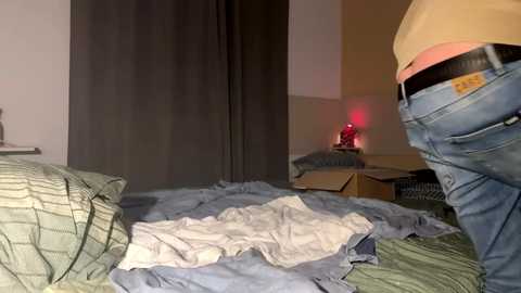 Media: Video of a messy bedroom with an unmade bed, partially open jeans, scattered clothes, and a small red statue on a wooden table.