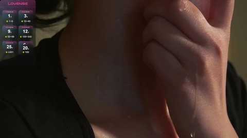 Close-up video of a person's hand lightly touching their neck, wearing a black top. Background shows a digital weather display with temperature, humidity, and wind speed readings.