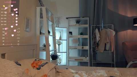 Media: Video of a cozy bedroom with a white bed, white shelves, and a wall-mounted TV displaying social media notifications. The room has a soft, warm ambiance with a mix of modern and minimalist decor.