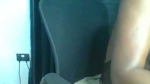 Video of a person's bare backside, partially obscured by a dark curtain, standing in a dimly lit room with a black electrical outlet visible on the left wall.