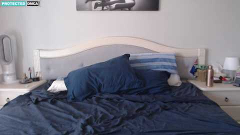 Media: A video of a neatly made bed with a blue comforter, two pillows, and a beige headboard in a modern, minimalist bedroom.