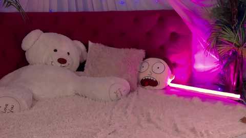 Media: Video of a plush bear and a large, cartoonish, red-faced creature on a white, fluffy rug in a dimly lit room with red walls and a pink glow.
