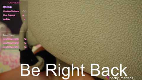 Video of a beige couch with a text overlay reading \"Be Right Back\" in white, accompanied by a blurred person in the background.
