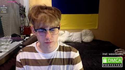 A video of a young boy with messy, light brown hair and glasses, wearing a striped shirt, sitting on a bed with a DMC logo.